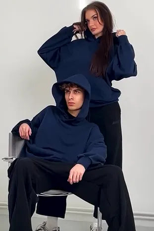 Two people wearing navy blue hoodies in a minimalistic setting