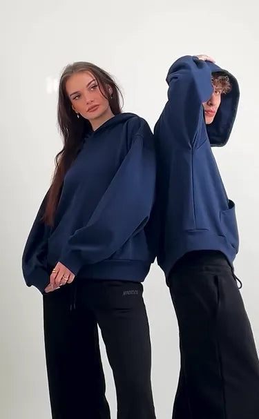 Two people wearing oversized navy blue hoodies and black pants on a white background
