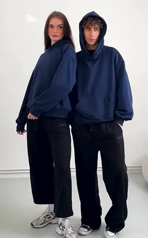 Two people wearing navy blue hoodies and black pants on a white background