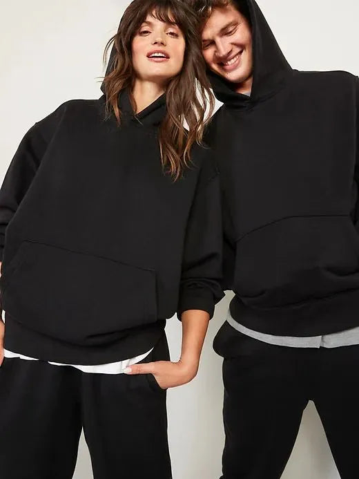 Two people wearing black hoodies and pants against a plain background