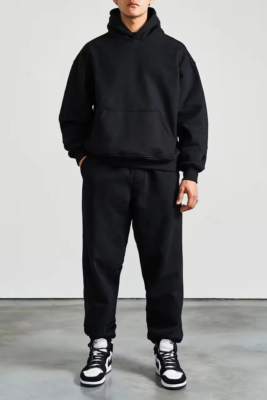 Person wearing a black hoodie and pants with black and white sneakers on a plain background