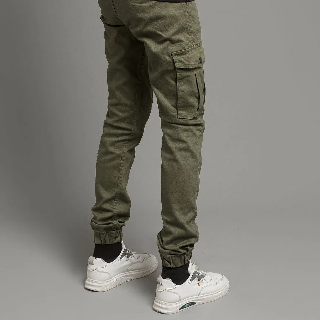 Person wearing green cargo pants and white sneakers on a gray background