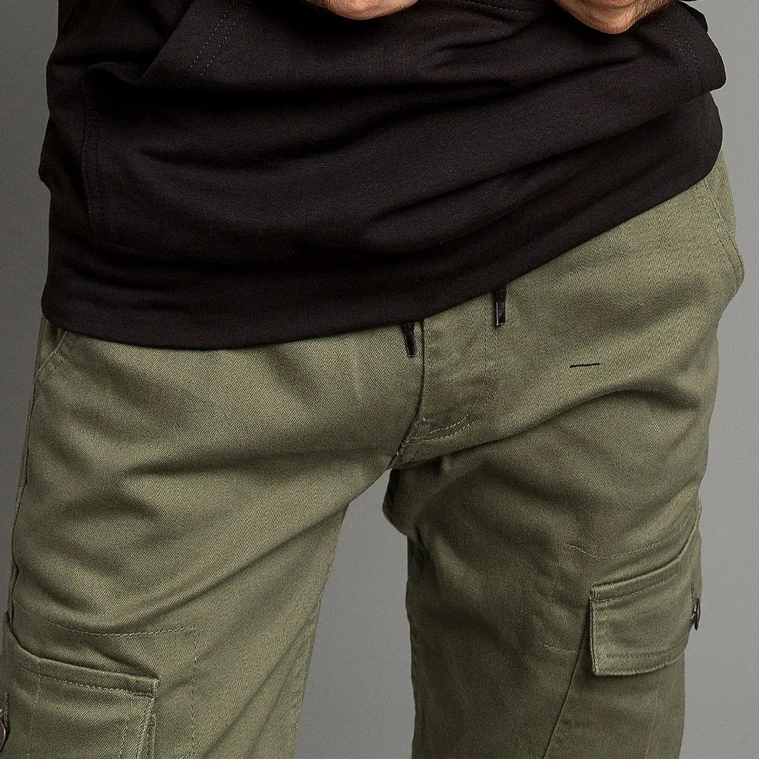 Person wearing olive green cargo pants and a black shirt on a gray background