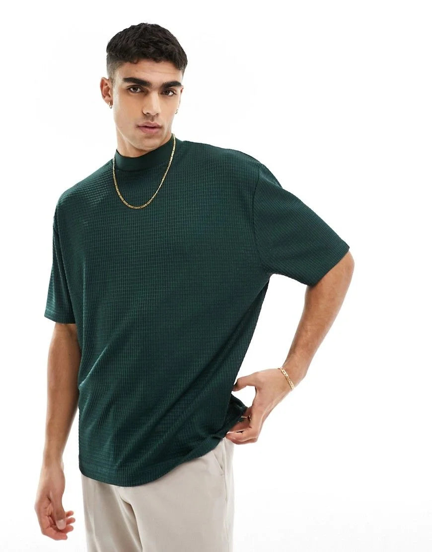 Man wearing a green turtleneck shirt and beige pants on a white background