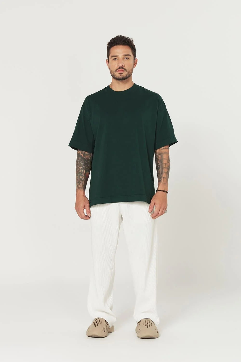 Man wearing a dark green t-shirt and white pants on a white background