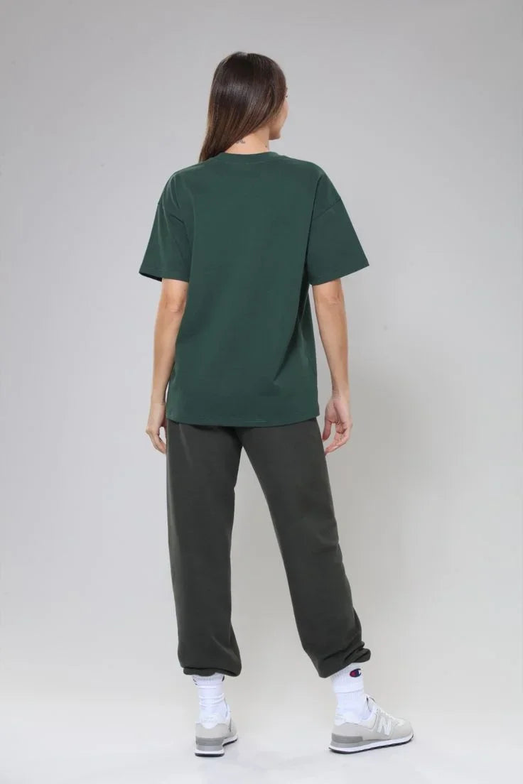 Person wearing a green t-shirt and dark pants on a plain background