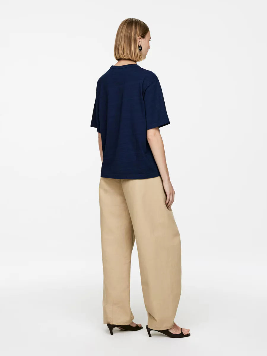 Woman wearing a navy blue top and beige pants on a white background